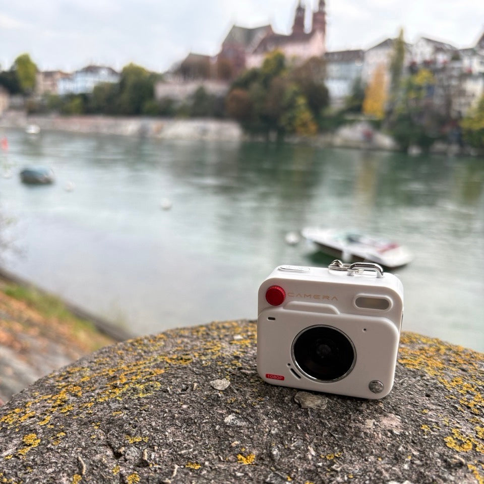 Camera-shaped object on a stone surface with a river and buildings in the background